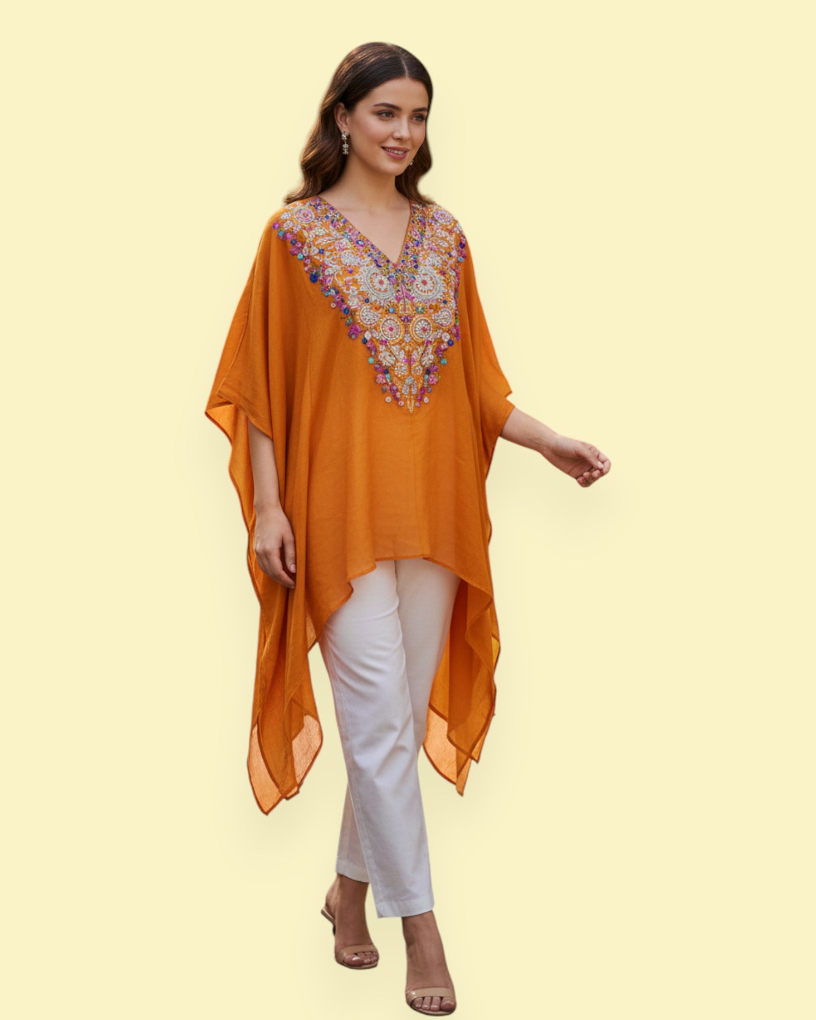Woman wearing an orange embroidered Kaftan and white pants on a light yellow background
