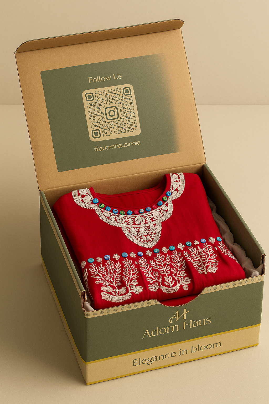 Red garment with white embroidery in a 'Adorn Haus' box on a beige background
