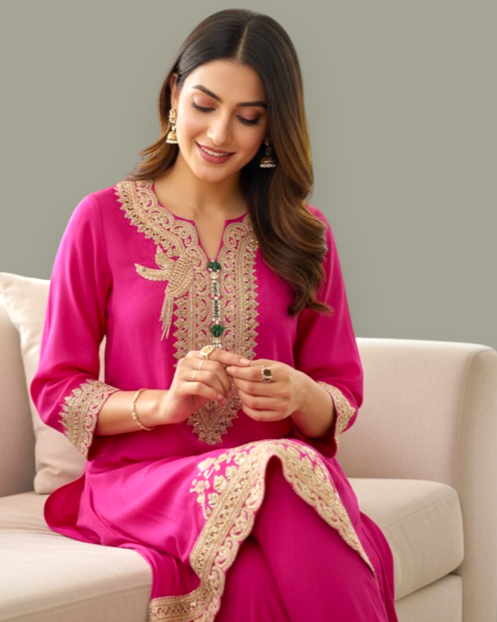 Woman wearing a pink embroidered traditional outfit sitting on a couch.