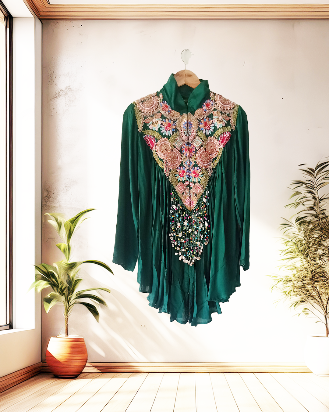 Green dress with floral embroidery on a wooden hanger against a light wall.
