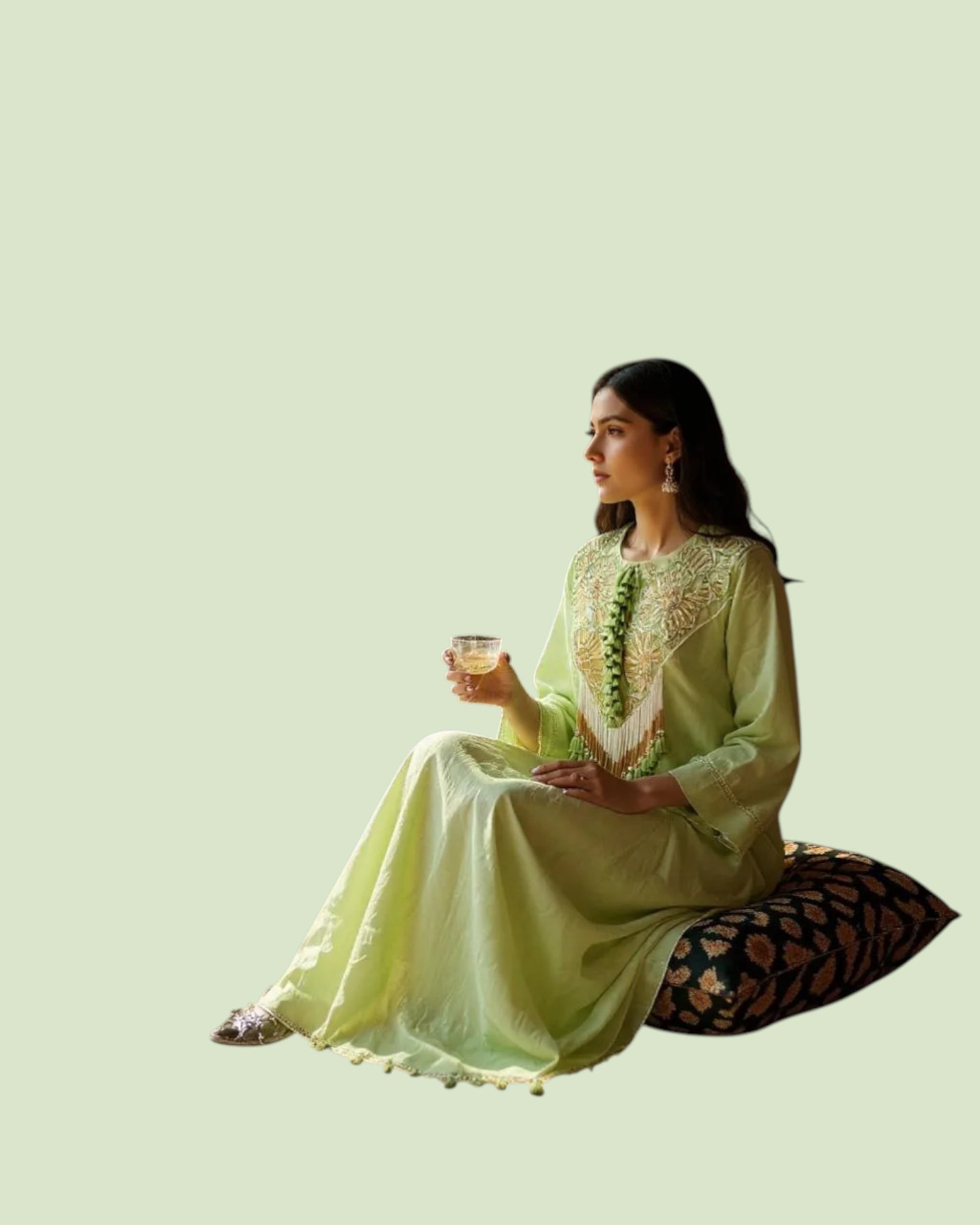 Woman in a light green traditional outfit sitting on a patterned cushion against a light green background