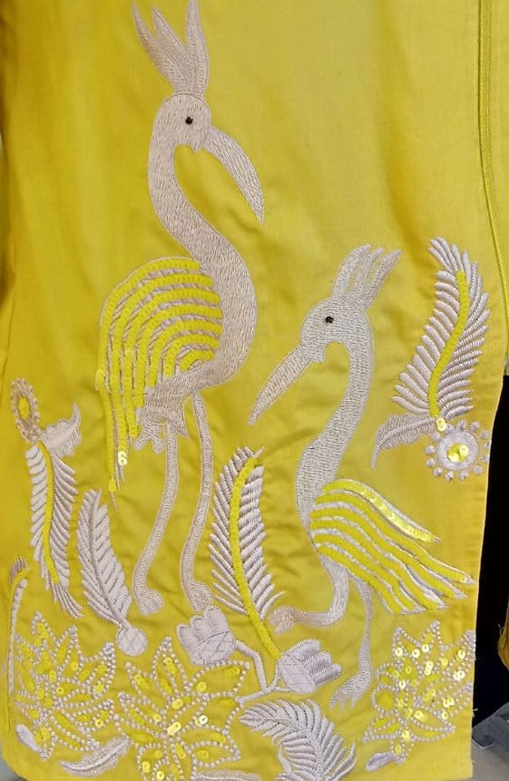 Embroidered design on a yellow fabric with birds and floral patterns.