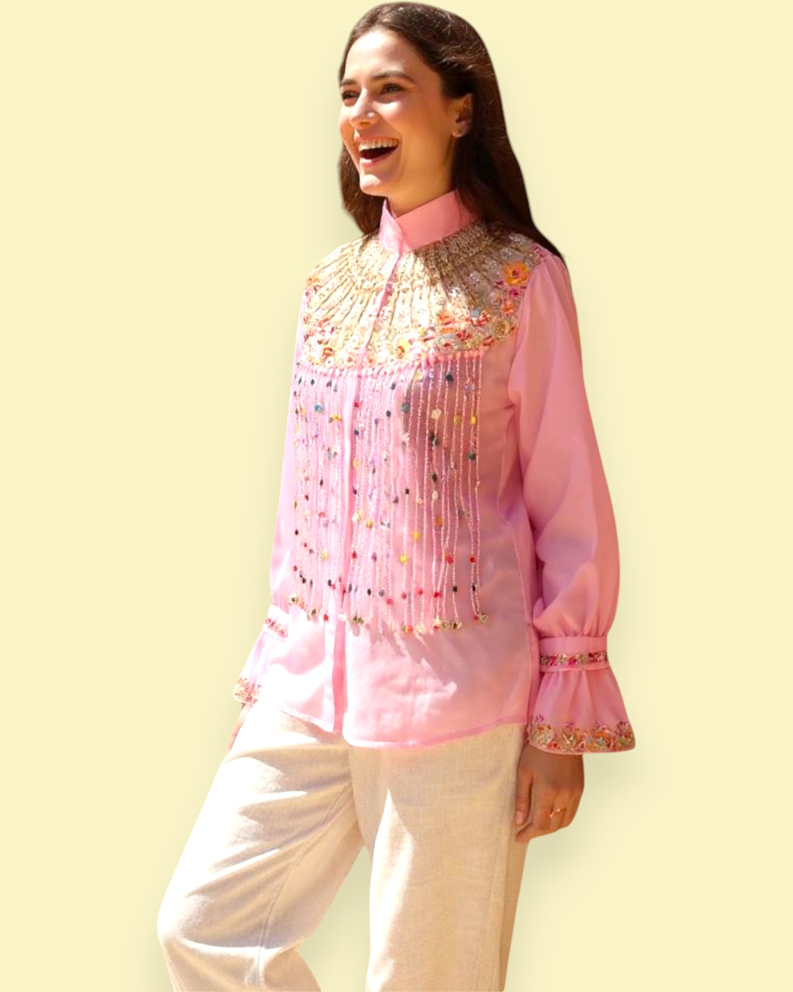 Woman wearing a pink embroidered Top with white pants on a light yellow background