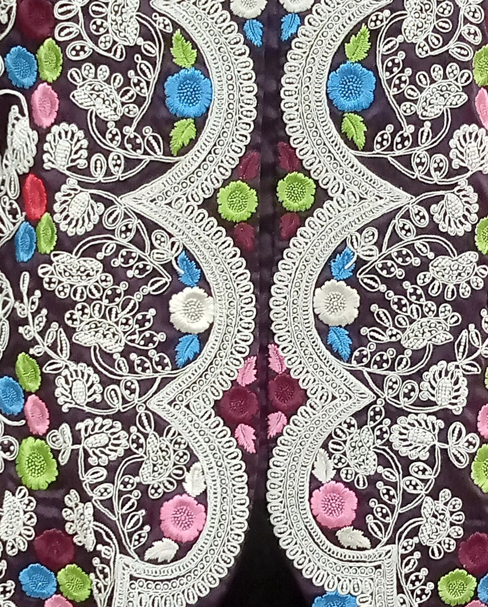 Close-up of intricate white lace with colorful floral embroidery on a dark background