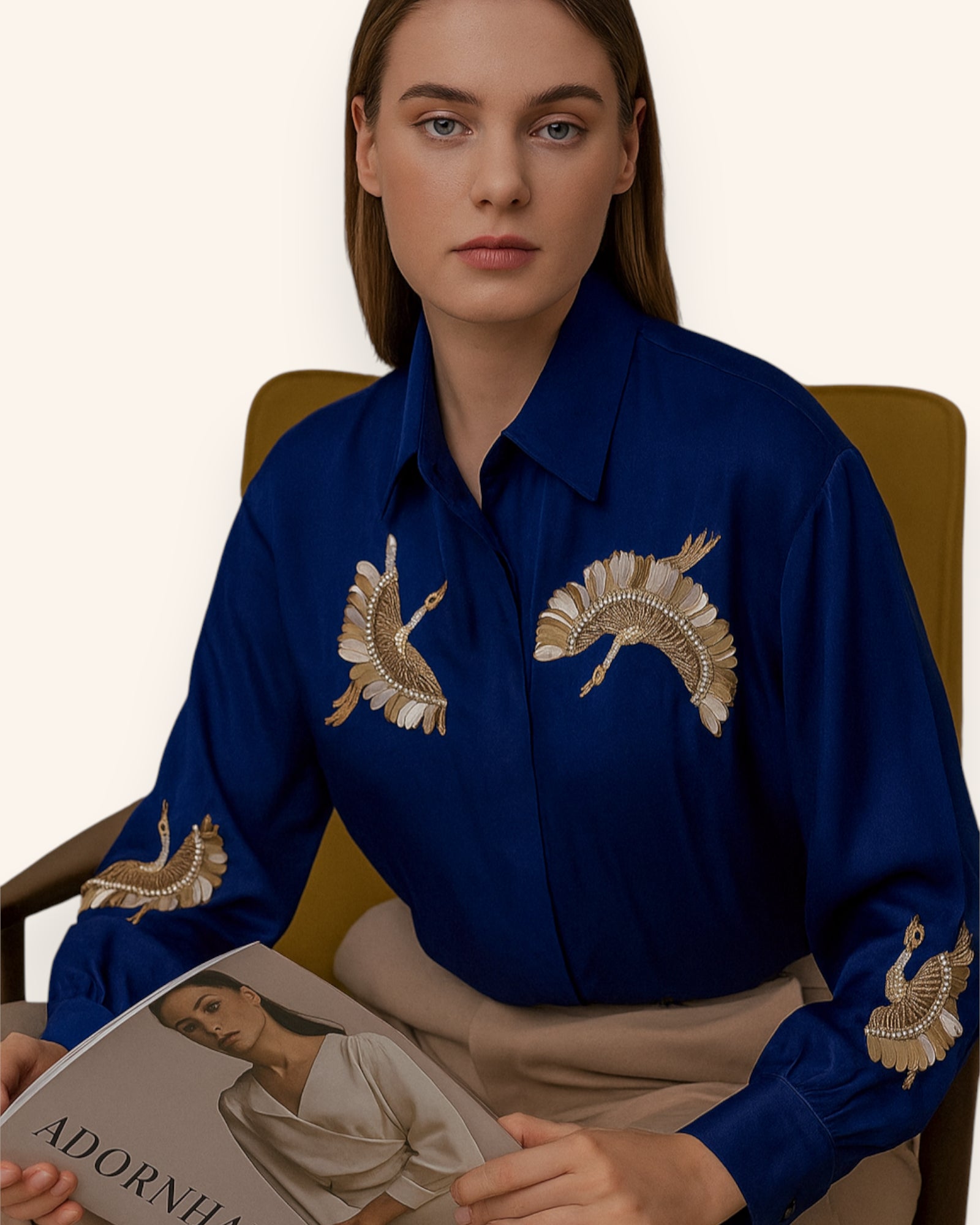 Woman wearing a blue shirt with gold bird embroidery, holding a magazine.