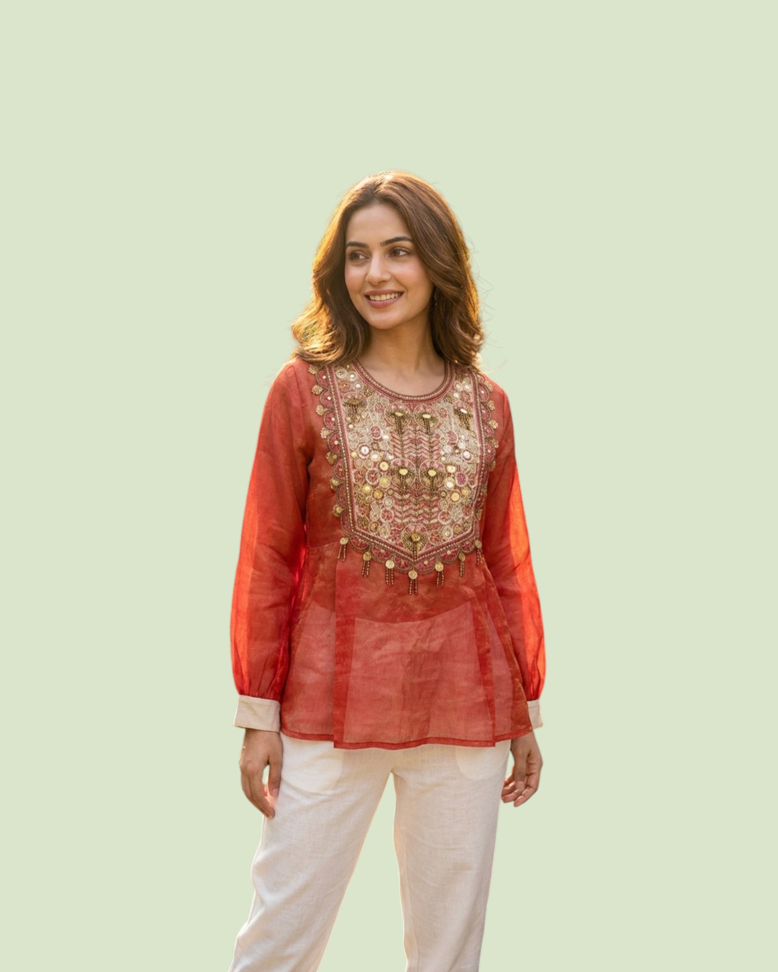 Woman wearing a red embroidered top with white pants on a light green background