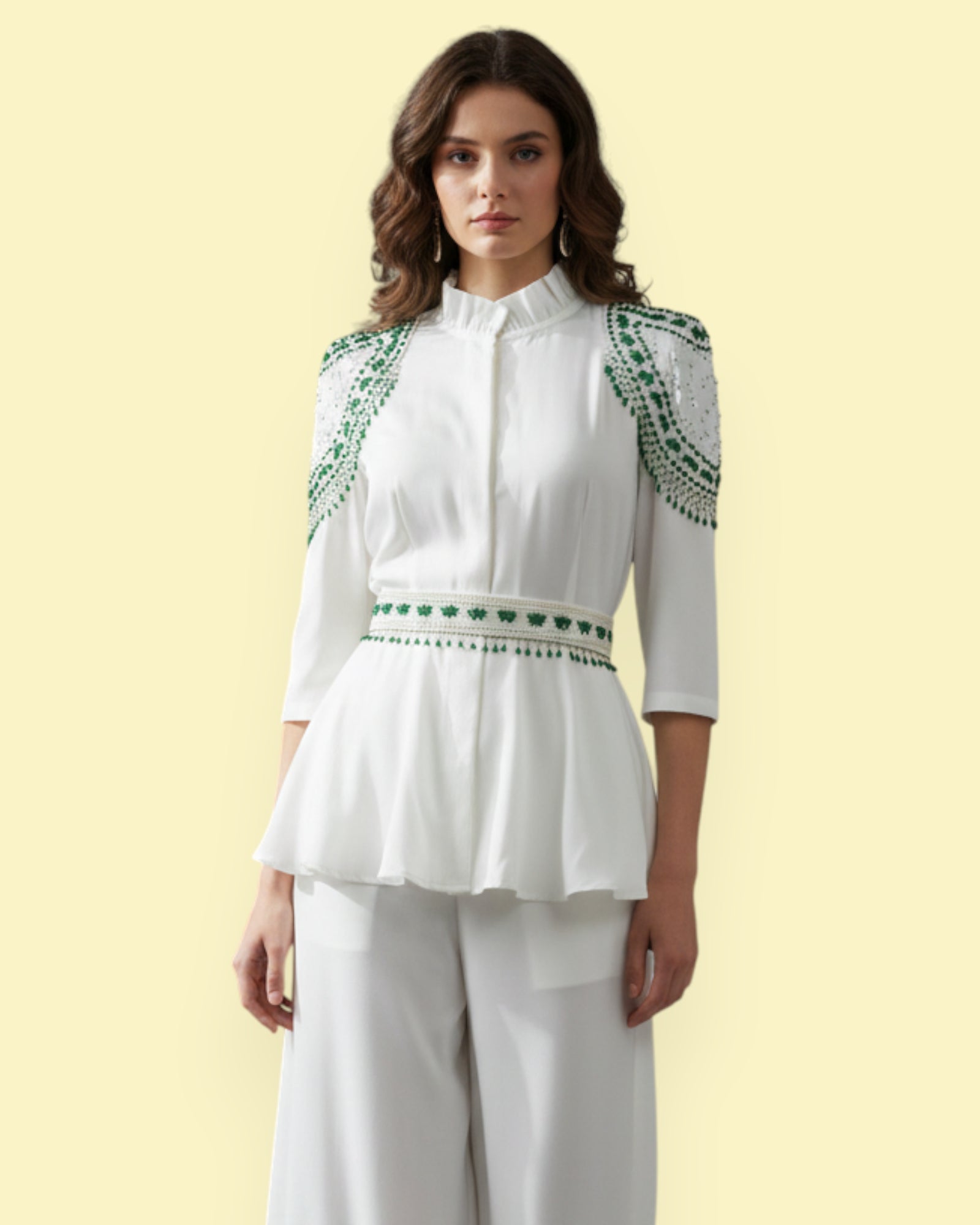 Woman wearing a white blouse with green embroidery on a light yellow background