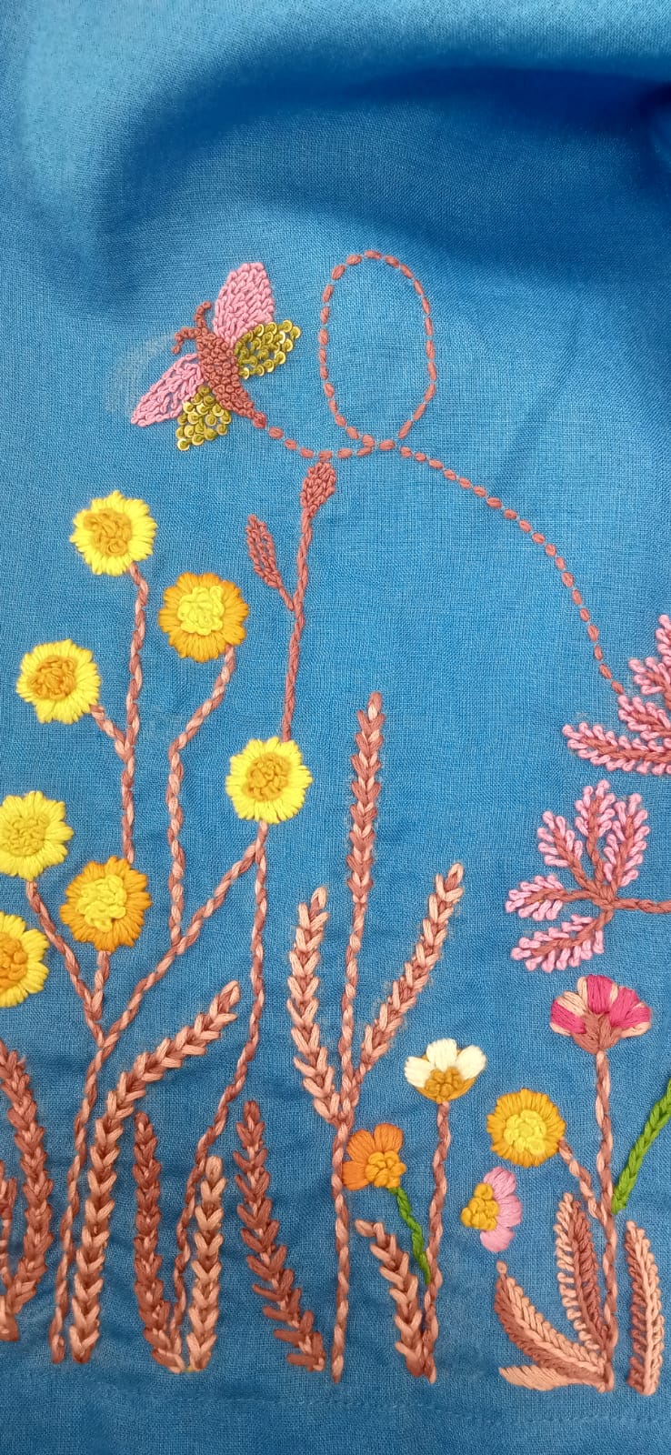 Embroidered design of a person with flowers and a butterfly on blue fabric