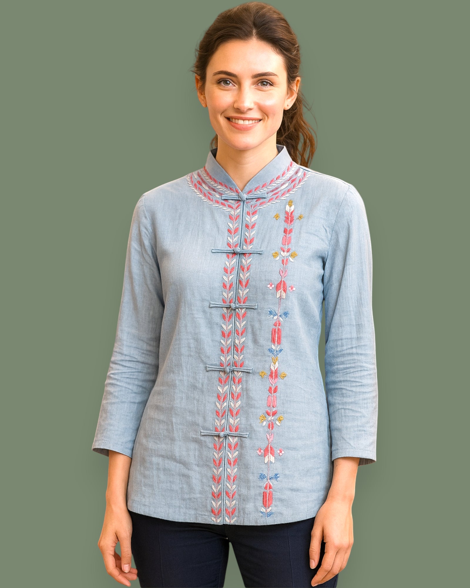Woman wearing a light blue embroidered shirt on a dark green background