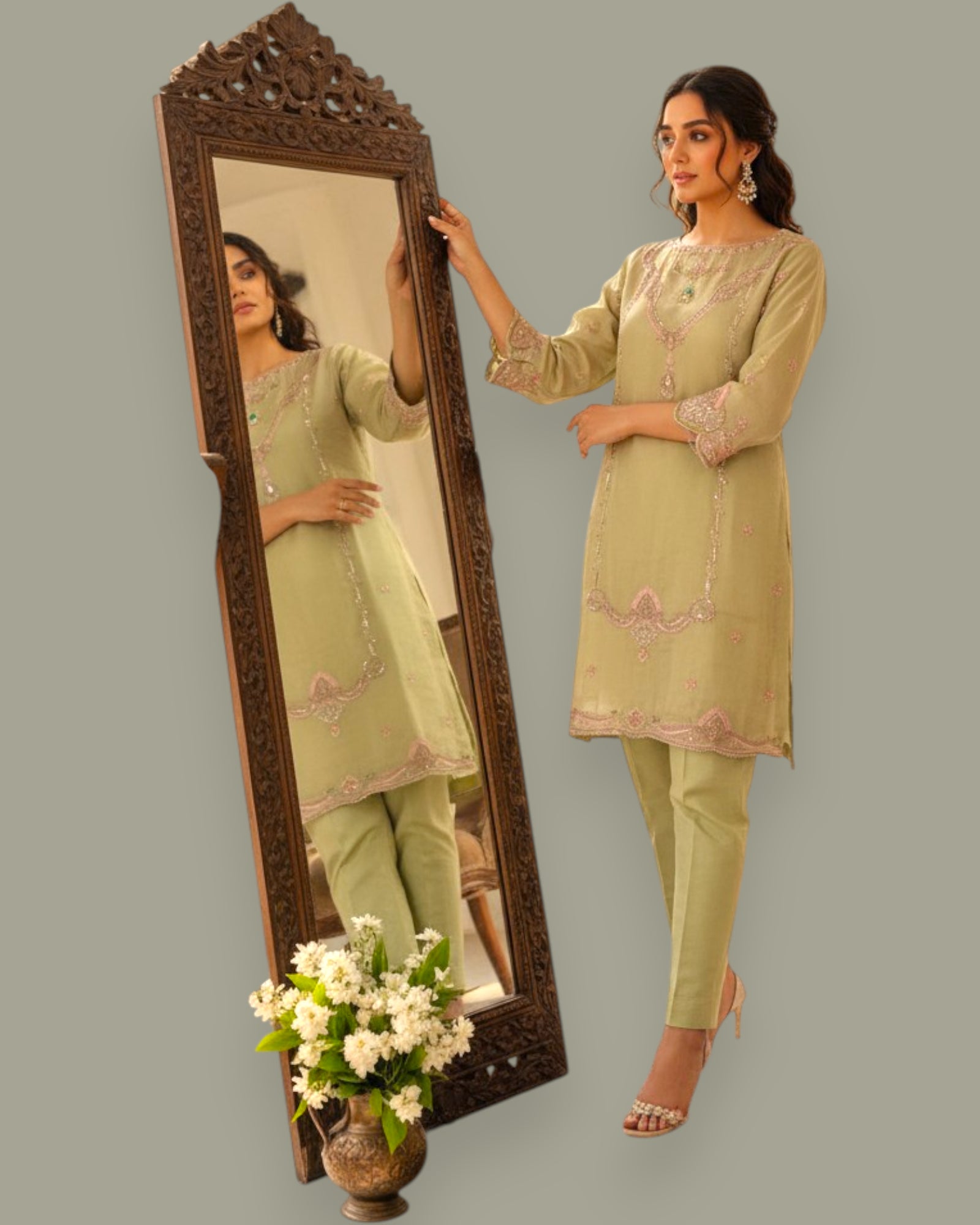 Woman in a light green traditional outfit standing next to a decorative mirror.