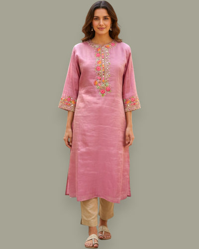 Woman wearing a pink embroidered kurta with beige pants on a gray background