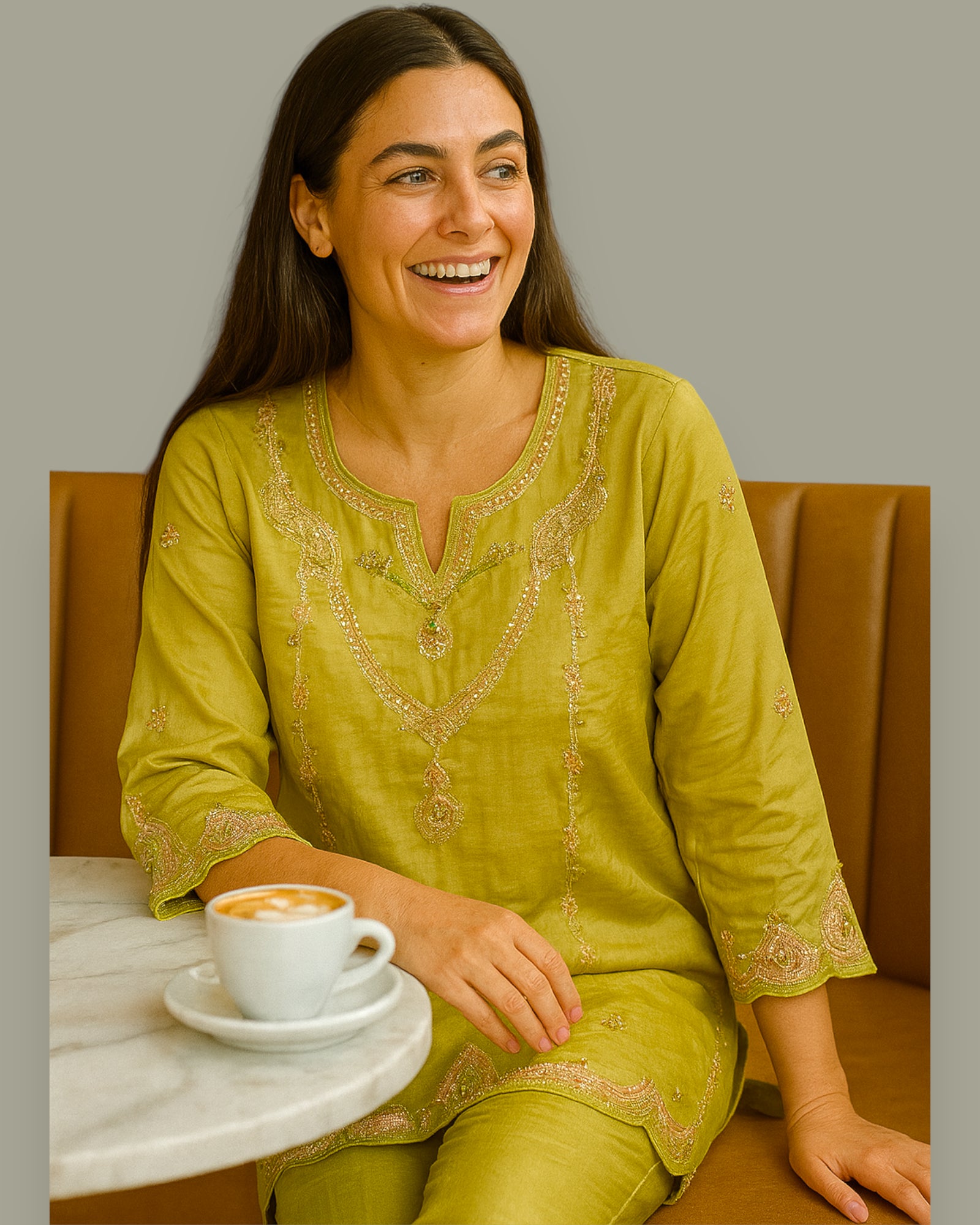 Woman in a green embroidered outfit sitting at a table with a cup of coffee.