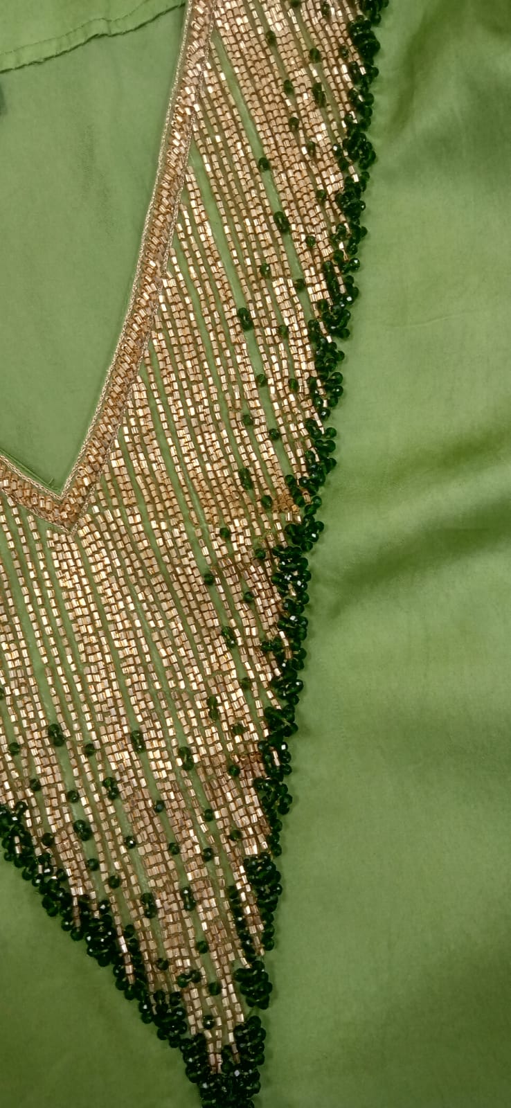 Close-up of a green garment with intricate beadwork on a matching green background