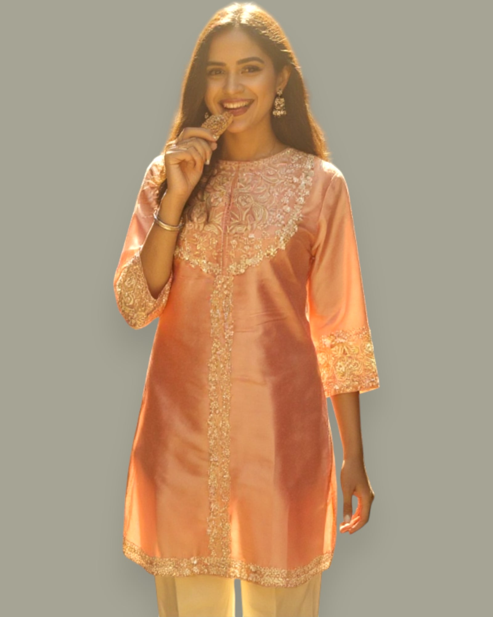 Woman wearing a peach-colored kurta with gold embroidery on a gray background