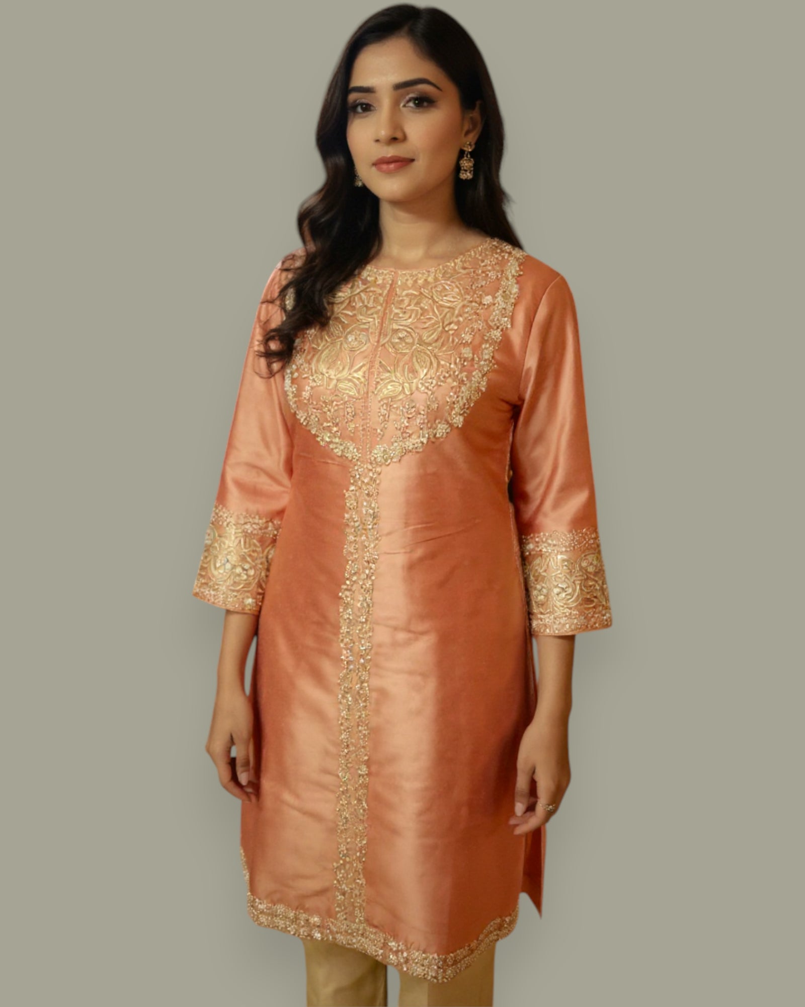 Woman wearing a peach-colored kurta with gold embroidery on a plain background