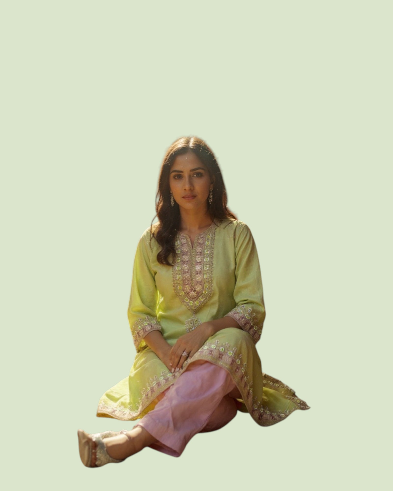 Woman wearing a light green and pink traditional outfit sitting on a light green background