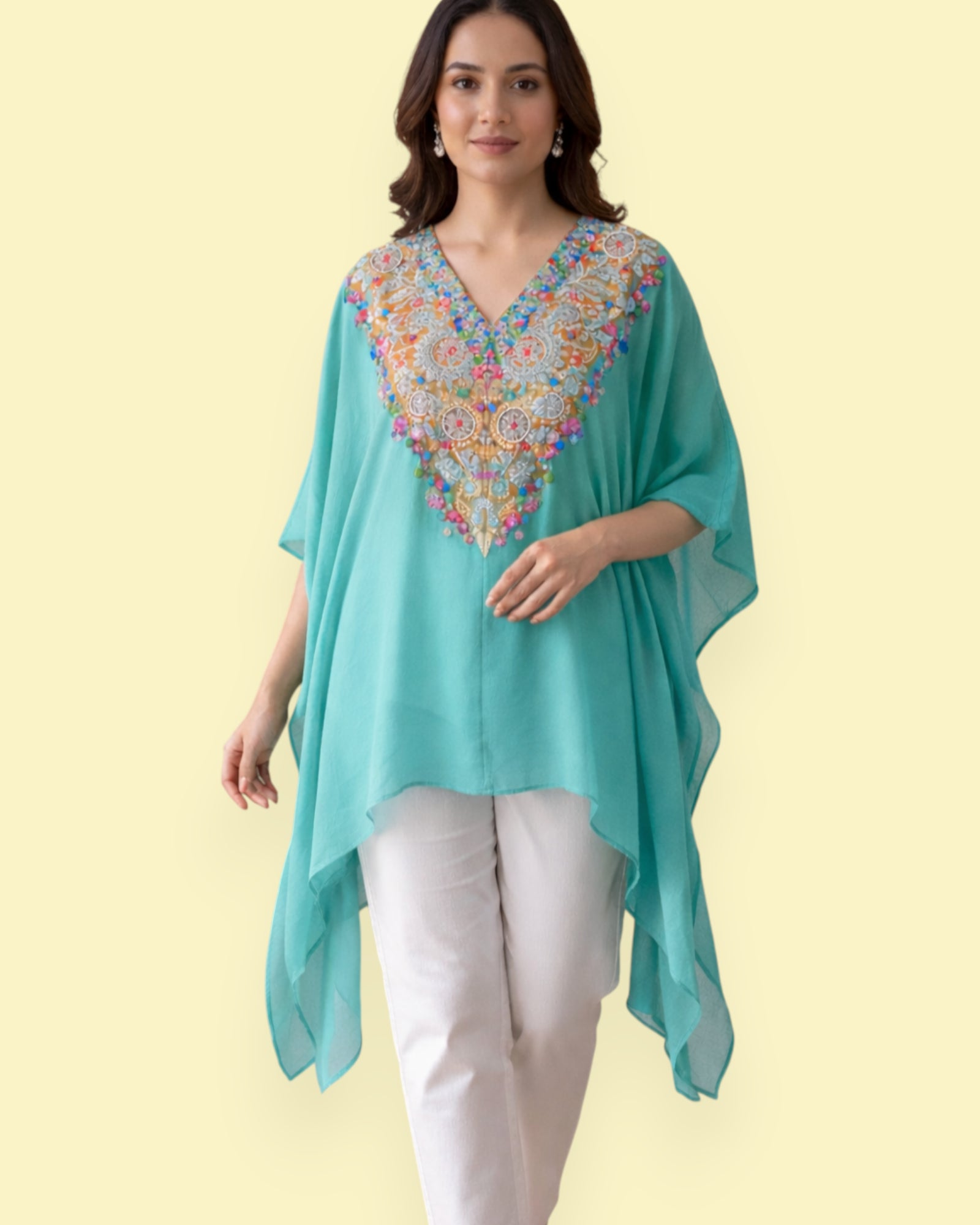 Woman wearing a turquoise Kaftan with colorful embroidery on a light yellow background