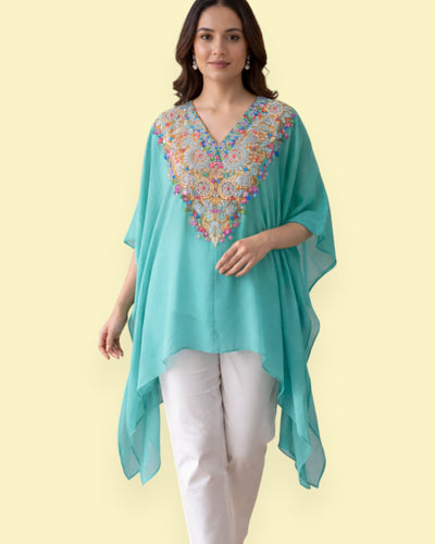 Woman wearing a turquoise Kaftan with colorful embroidery on a light yellow background