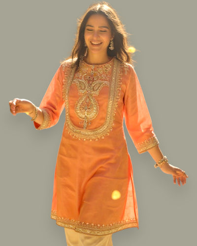 Woman wearing an Peach embroidered kurta against a gray background