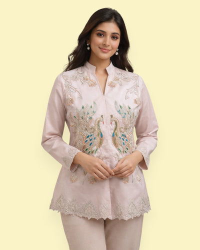 Woman wearing a light pink embroidered Jacket with a plain background