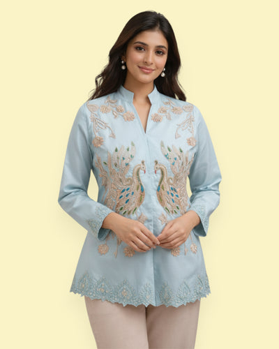 Woman wearing a light blue embroidered Jacket with peacock designs on a beige background