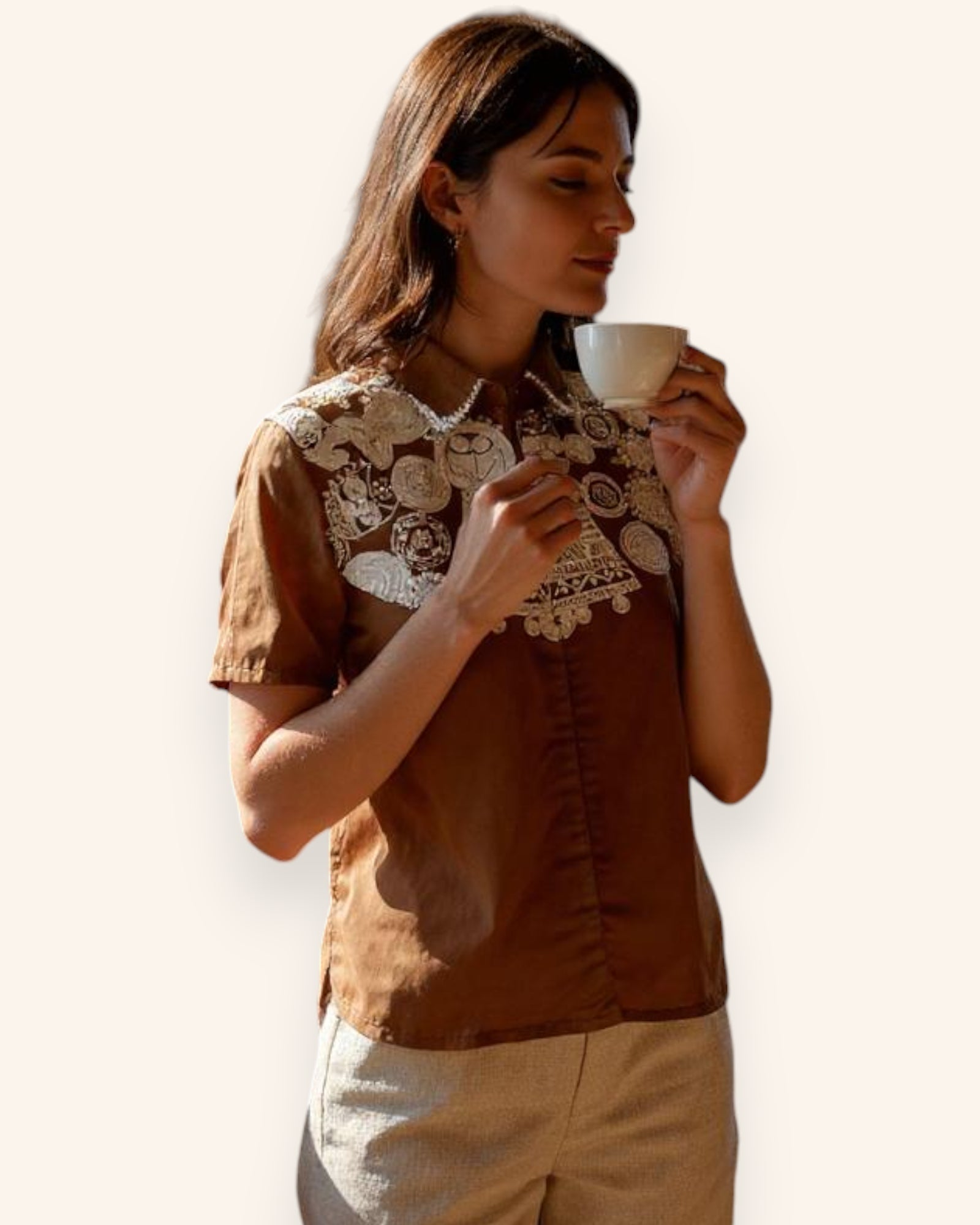 Woman wearing a brown Shirt with lace details, holding a cup against a plain background