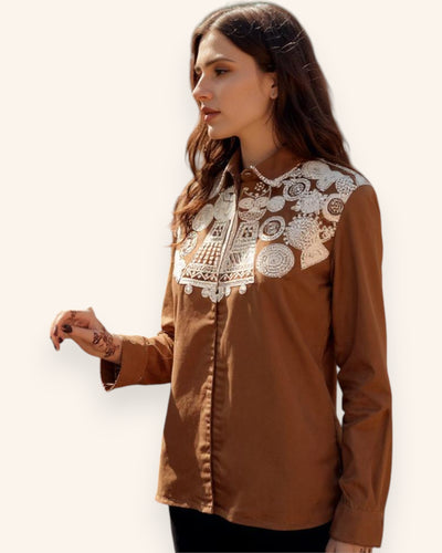 Woman wearing a brown Shirt with white lace detailing on a plain background