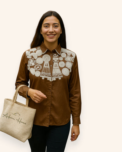 Woman wearing a brown Shirt with white embroidery, holding a beige tote bag with 'African Home' branding.