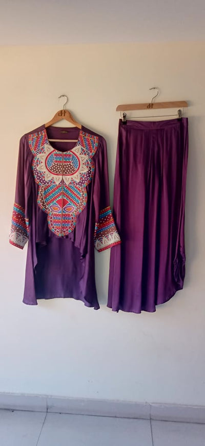 Purple outfit with embroidered top and pants hanging on a white wall.