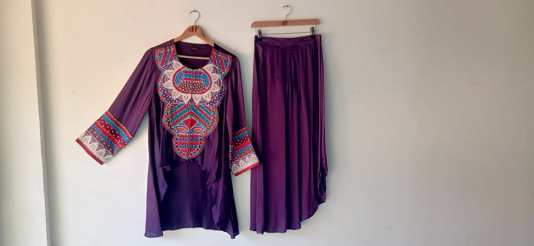 Purple embroidered top and skirt set on hangers against a white wall