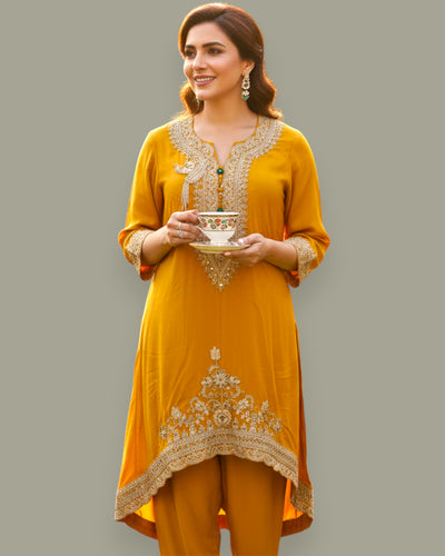 Woman wearing a mustard yellow embroidered outfit holding a decorative bowl against a gray background