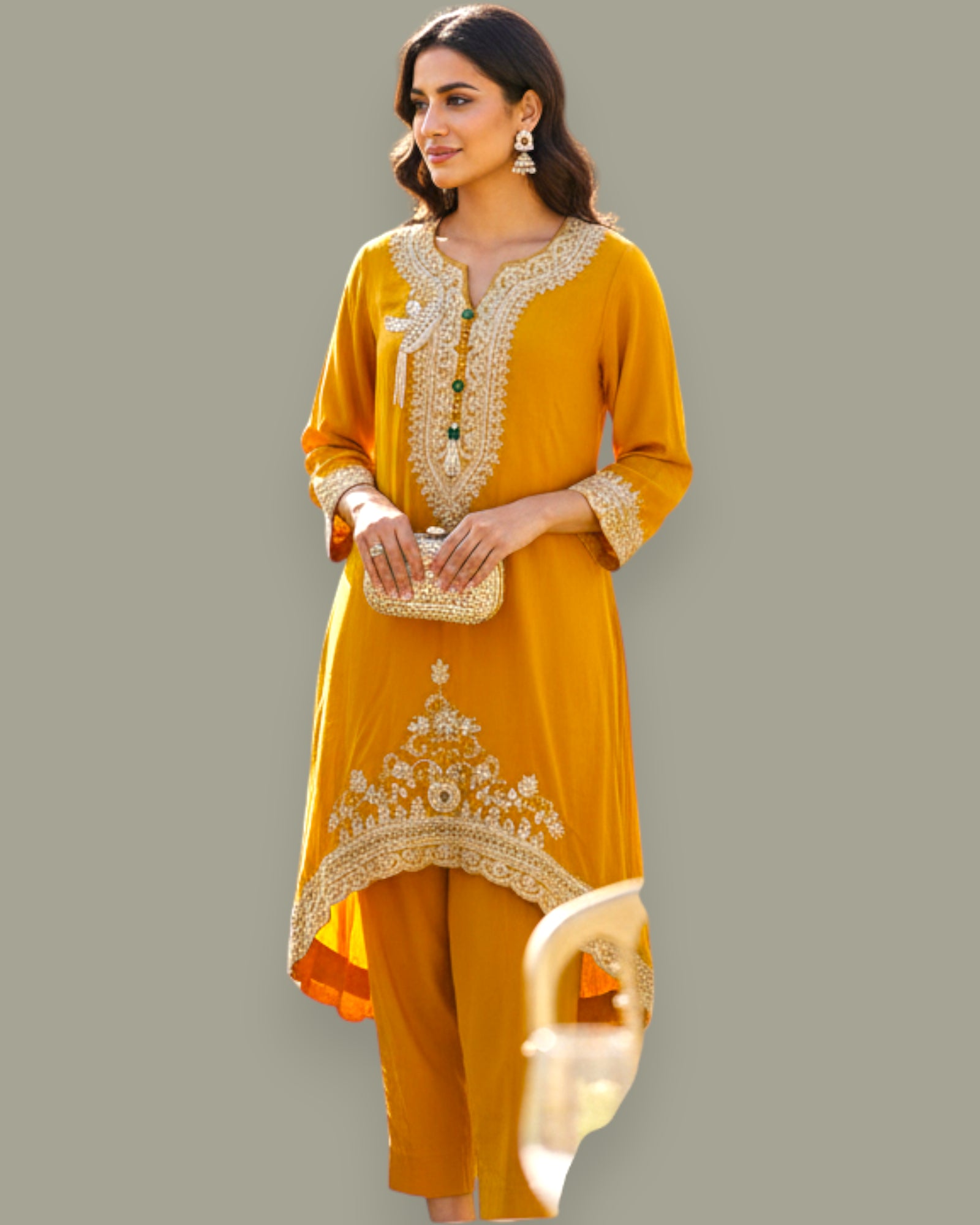 Woman wearing a mustard yellow traditional outfit with intricate embroidery on a gray background