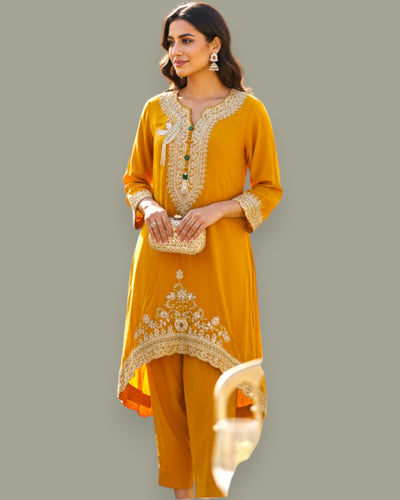 Woman wearing a mustard yellow traditional outfit with intricate embroidery on a gray background