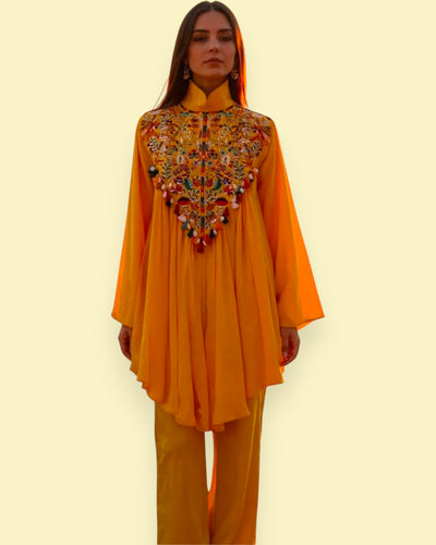Woman wearing a mustard yellow embroidered top and pants on a light beige background