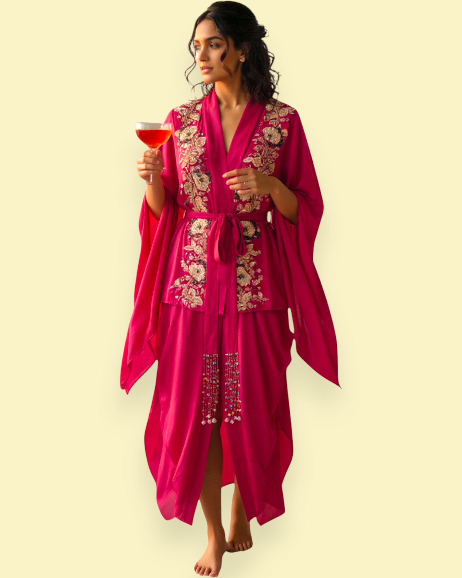 Woman in a pink embroidered outfit holding a tea against a beige background