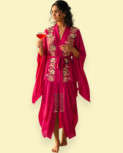 Woman in a pink embroidered outfit holding a tea against a beige background