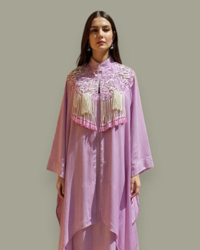 Woman wearing a pink embroidered dress with tassels on a plain background