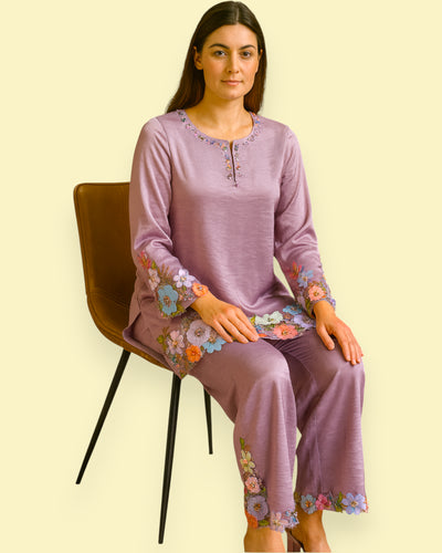 Woman wearing a purple embroidered outfit sitting on a chair against a beige background