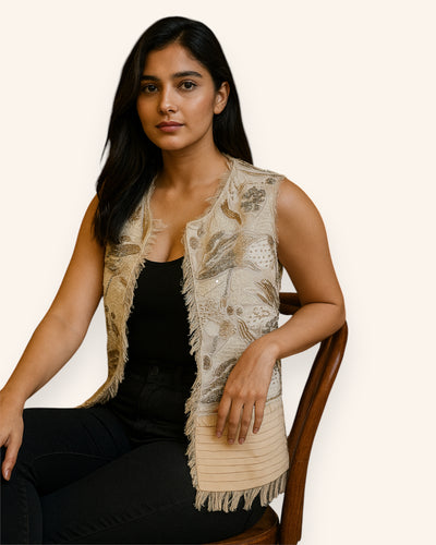 Woman wearing a Embroidery beige vest over a black top, sitting on a chair.