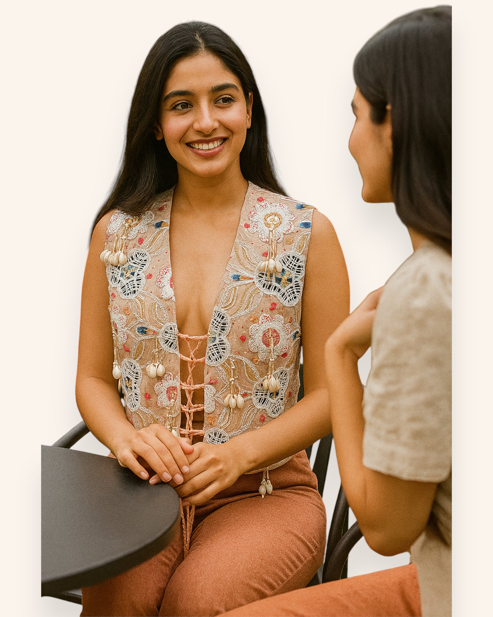 Woman wearing a Embroidery Vest and brown pants sitting at a table with another person.