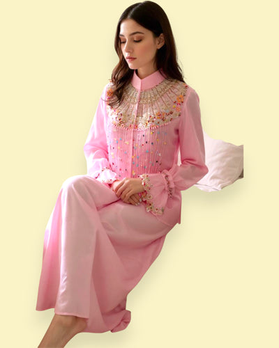 Woman wearing a pink traditional outfit with floral embroidery on a light yellow background