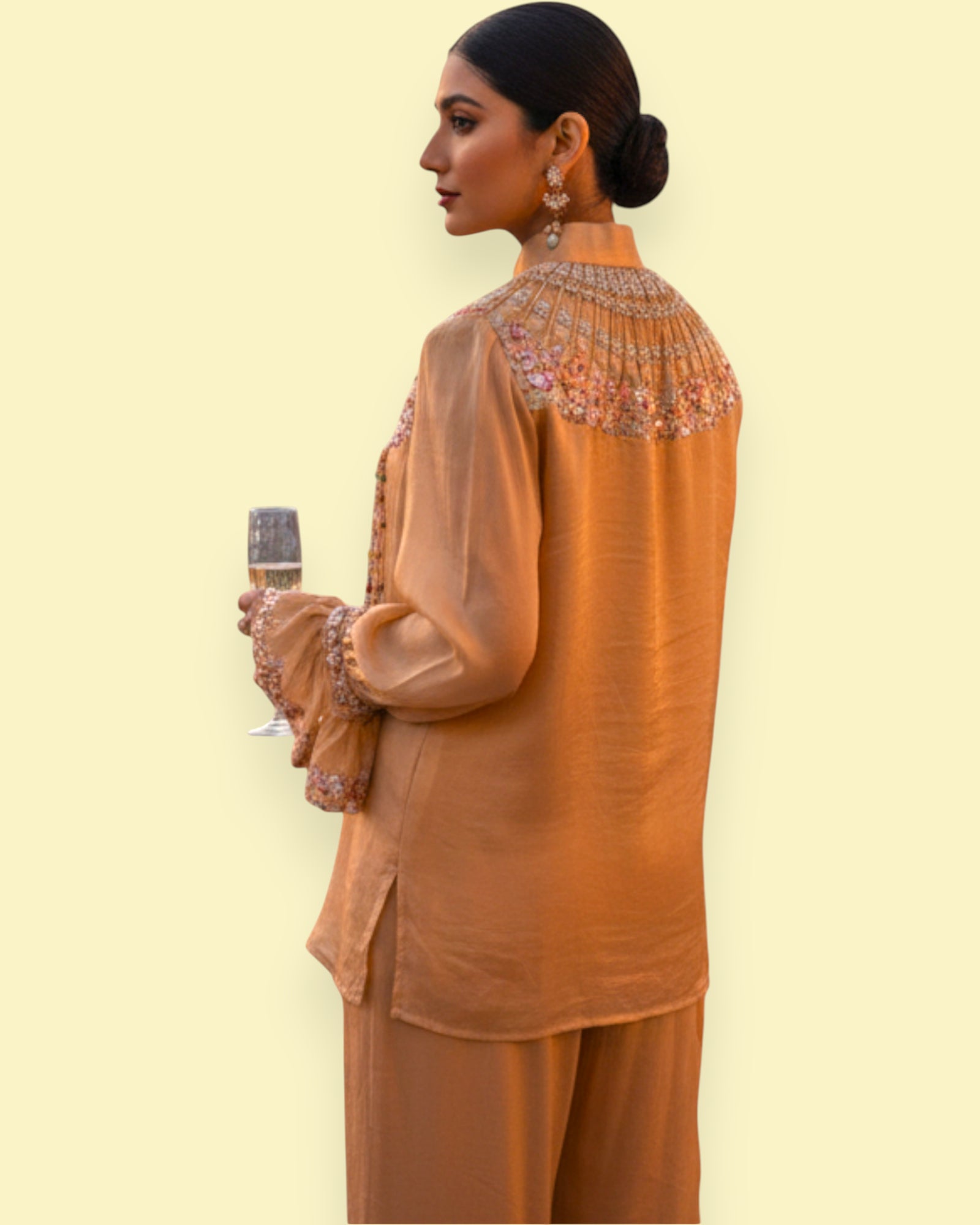 Woman wearing a brown traditional outfit with intricate detailing on a light yellow background