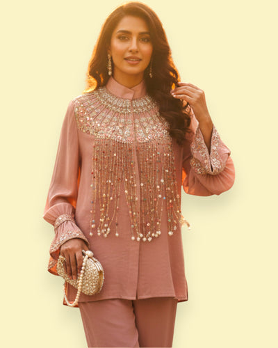 Woman wearing a pink traditional outfit with embellishments on a light yellow background