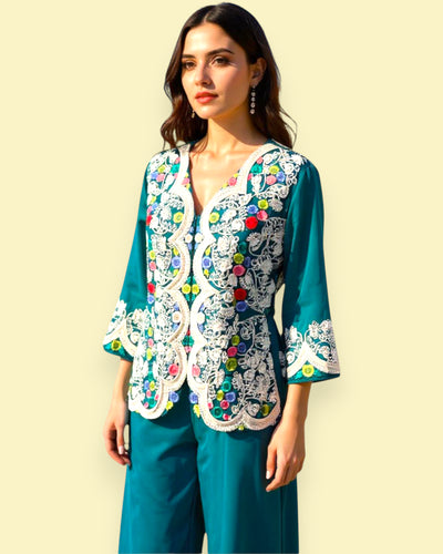 Woman wearing a teal outfit with colorful Embroidery against a light yellow background