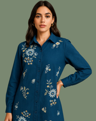 Woman wearing a blue embroidered shirt against a green background