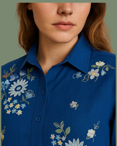Close-up of a blue shirt with floral embroidery on a plain background