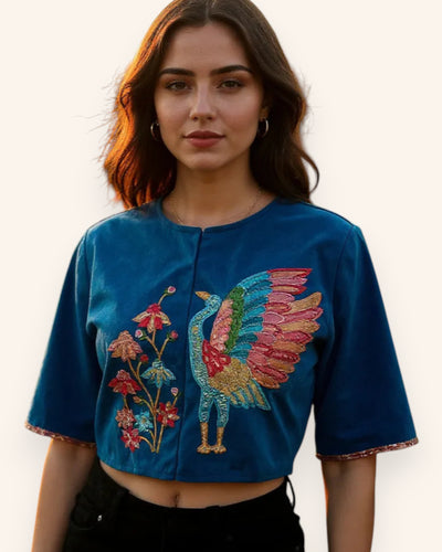 Woman wearing a blue embroidered top jacket with a colorful bird design on a plain background