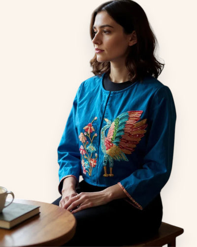 Woman wearing a blue embroidered Jacket with a colorful design, sitting at a table.