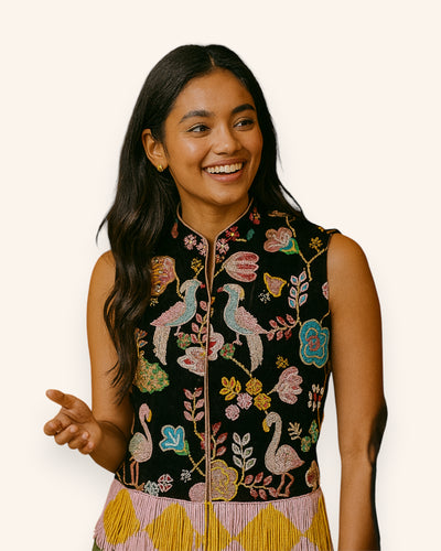 Woman wearing a black embroidered vest with colorful floral and bird patterns on a white background