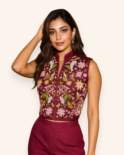 Woman wearing a maroon embroidered top with floral patterns on a plain background